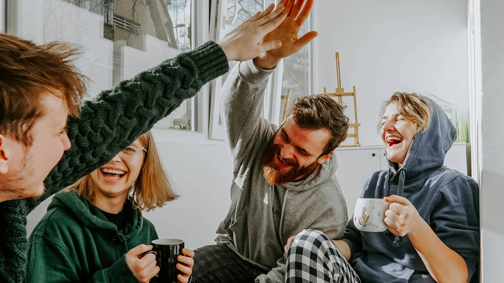 Un grupo de amigos jóvenes riendo y chocando la mano en el salón de su piso compartido